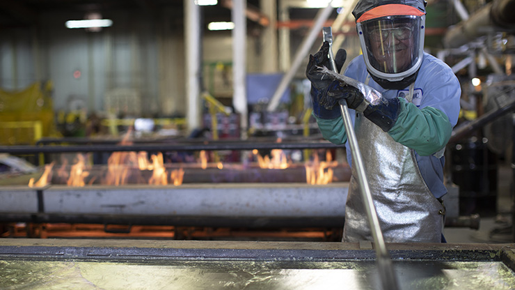 An employee skims dross off hot, liquid lead as a part of the metal refining process.